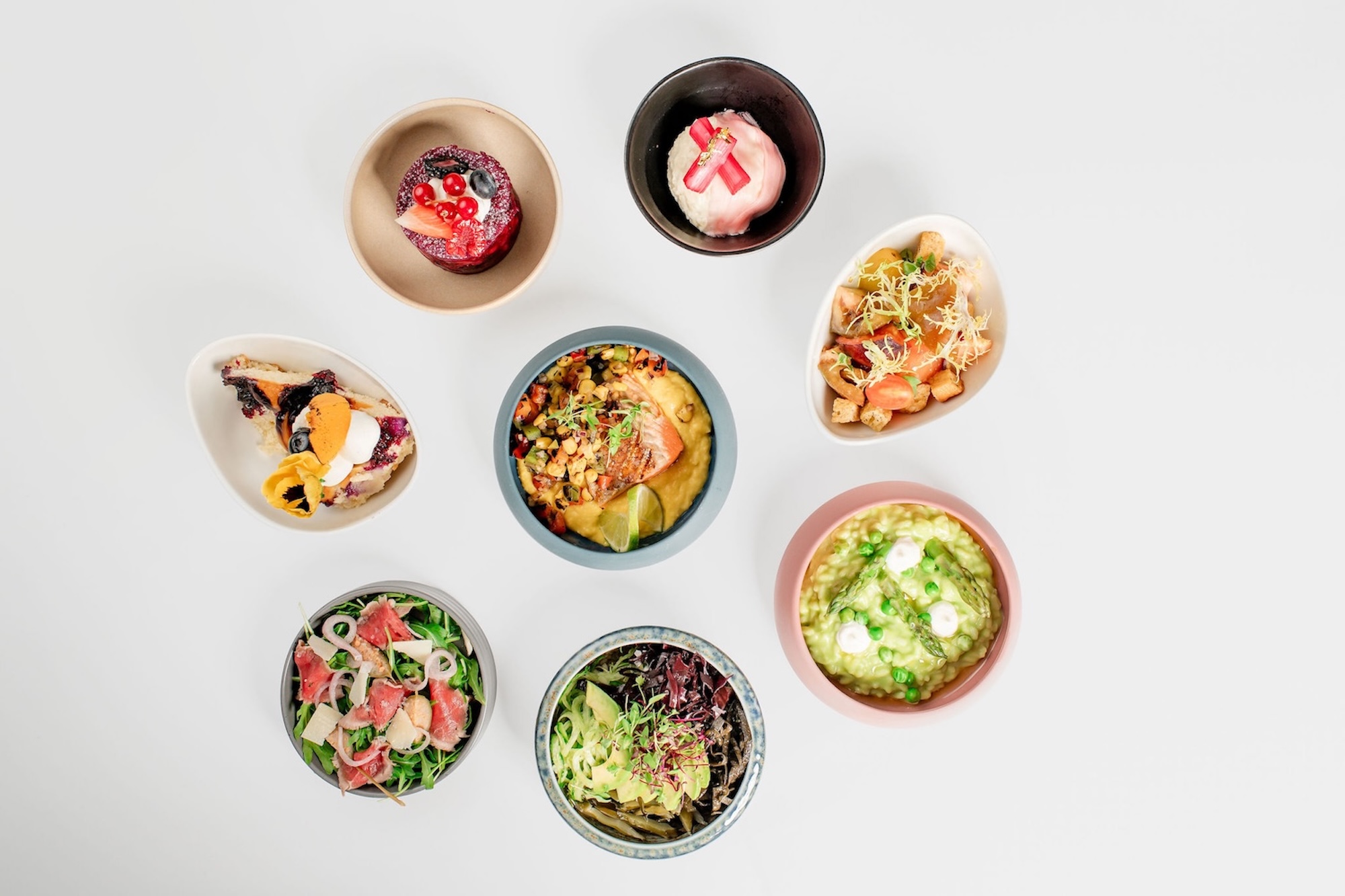 8 bowls of colourful food options, including risotto, salads and desserts. The bowls are neatly presented and arranged in a circle.